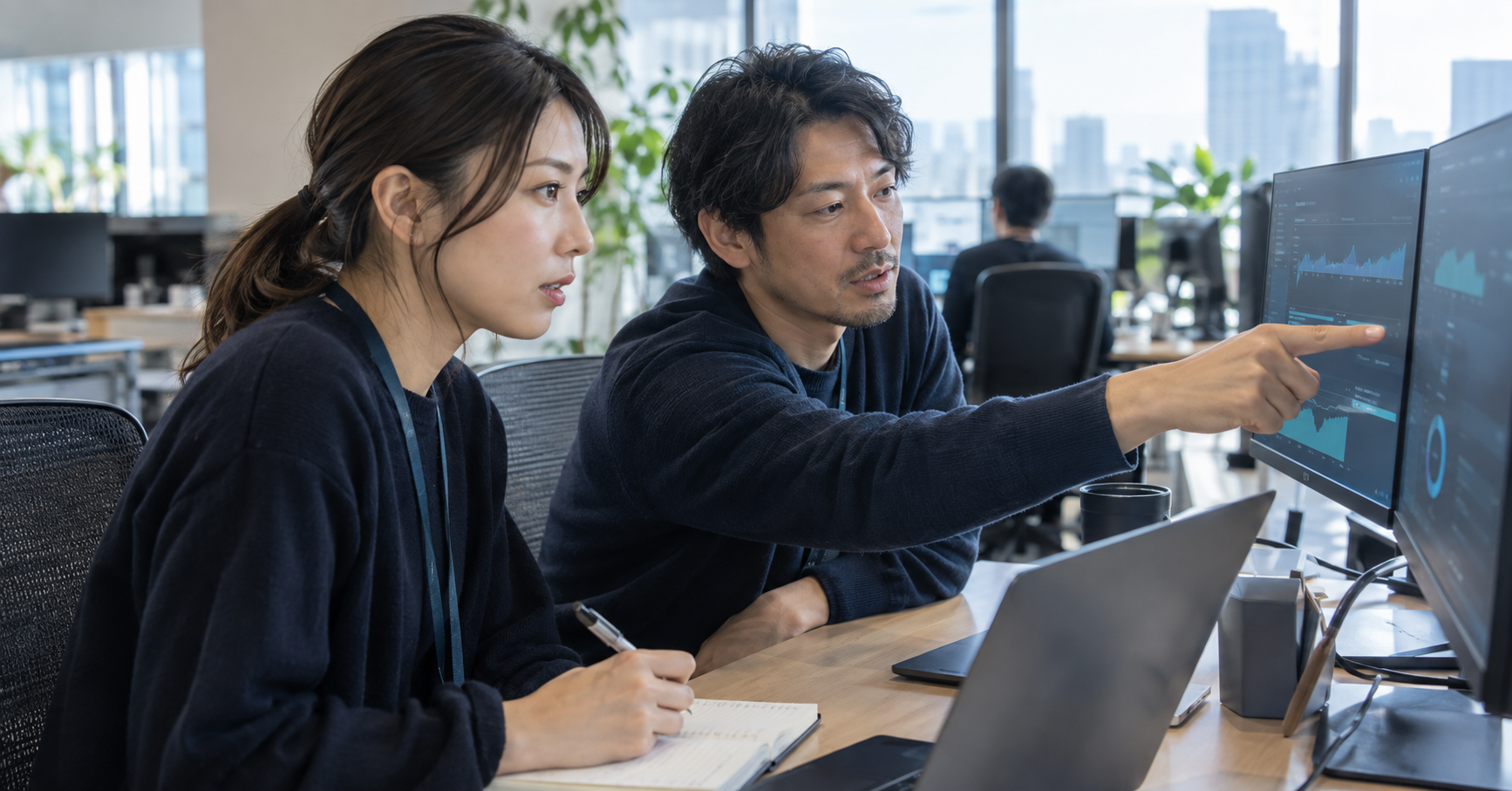 サービスの状態を示す画面を同僚と確認し、改善点を整理するエンジニアの実写風イメージ(AI生成)